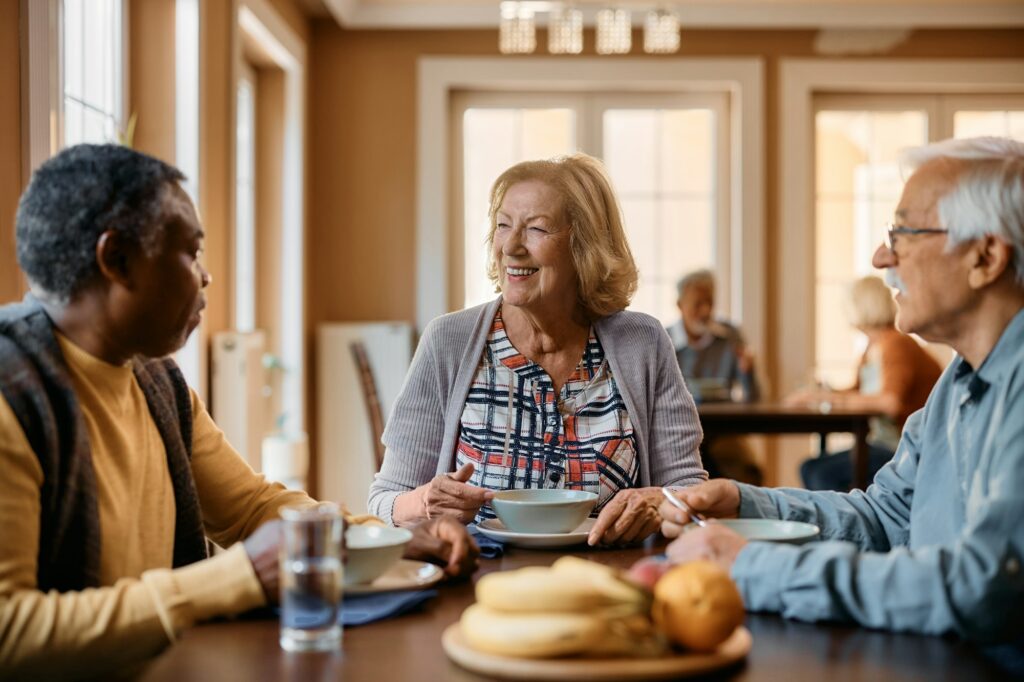 Happy senior woman and her friends communicating during a meal at residential care home.